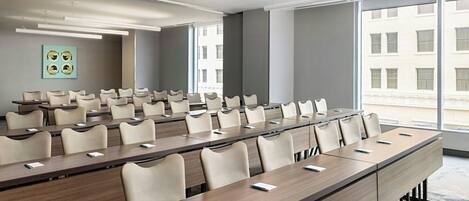 A conference room with long tables and chairs, large windows, and a modern ceiling design.