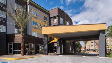 A modern hotel entrance with a covered walkway, palm trees, and a clear sky.