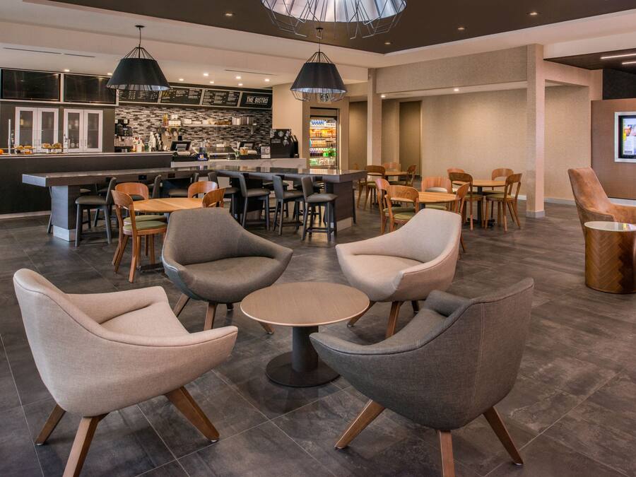 Un espace de détente moderne, doté de sièges confortables, d’un bar et d’un écran numérique affichant des informations.