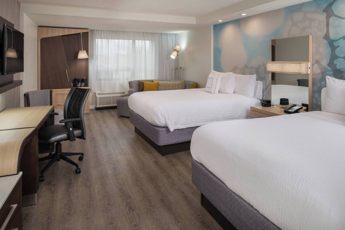 A hotel room with two beds, a desk, a chair, a TV, and a large mirror.