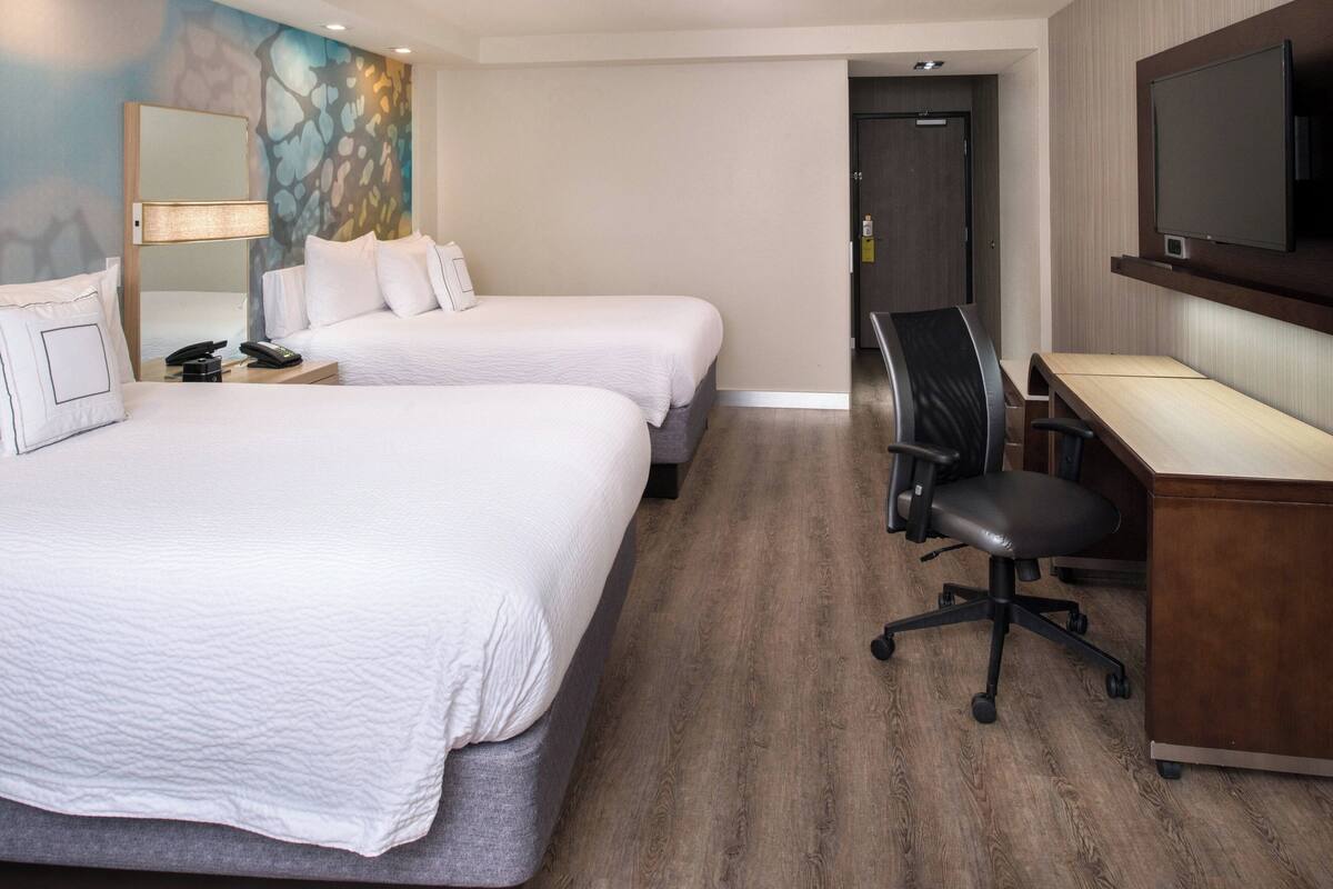 A hotel room with two beds, a desk, a chair, a TV, and a mirror.