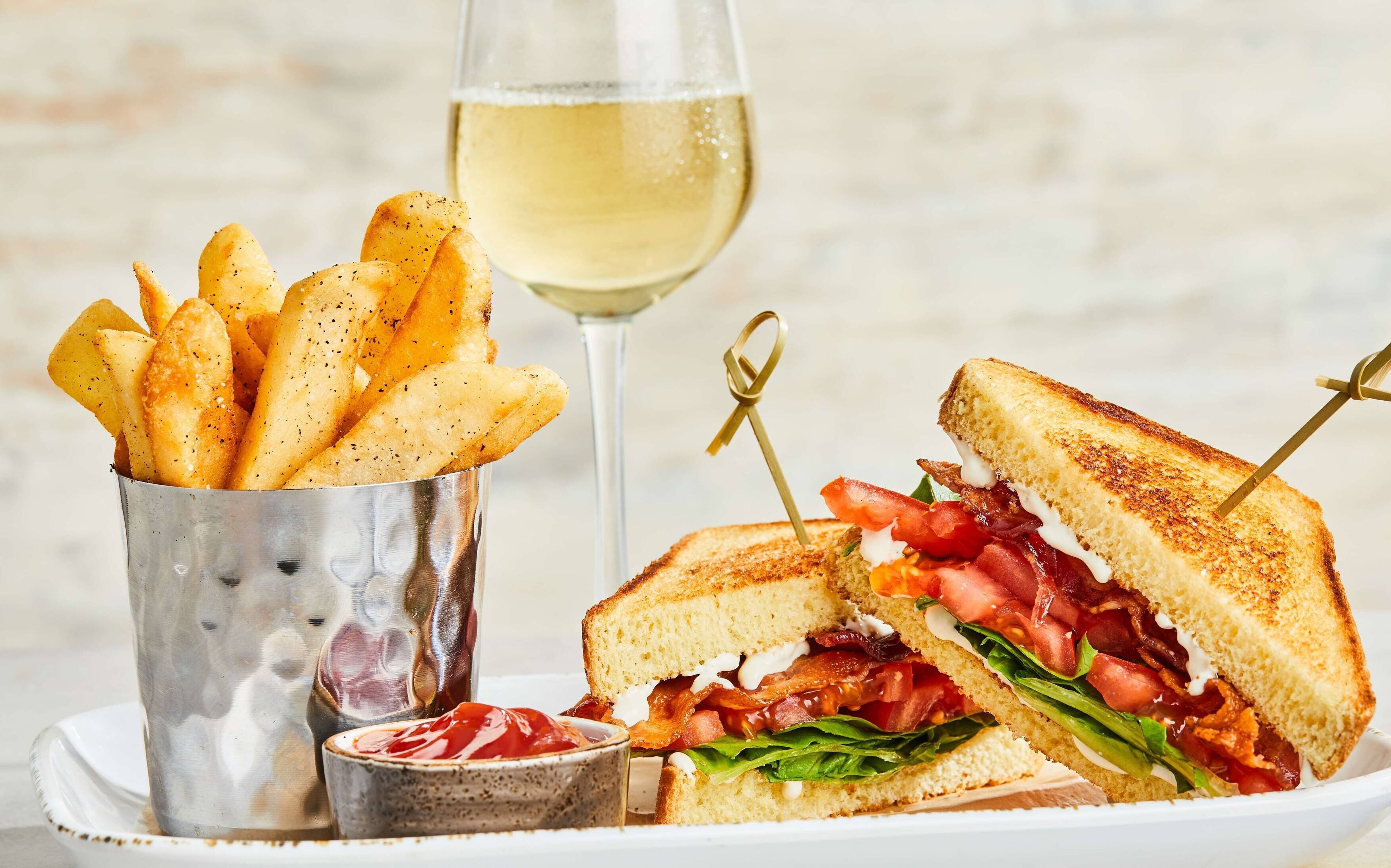 Un sandwich accompagné d’une portion de frites et d’un verre de vin blanc.