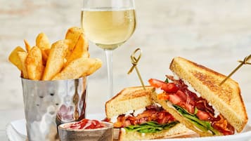 Un sandwich accompagné d’une portion de frites et d’un verre de vin blanc.