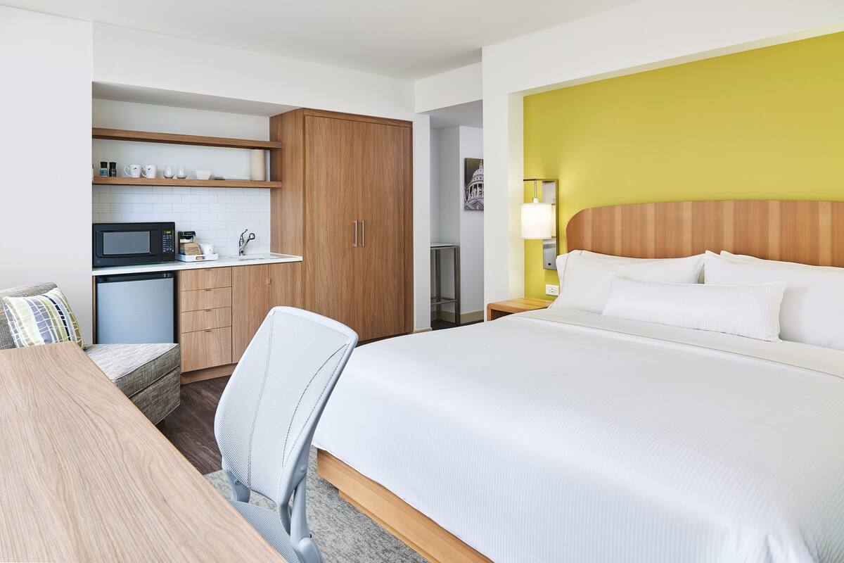 Una habitación de hotel con una cama, un escritorio, un microondas, una cafetera y un armario.
