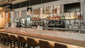 A bar area with a long counter, multiple stools, and shelves stocked with various bottles. - Element by Marriott Austin Downtown (Austin)