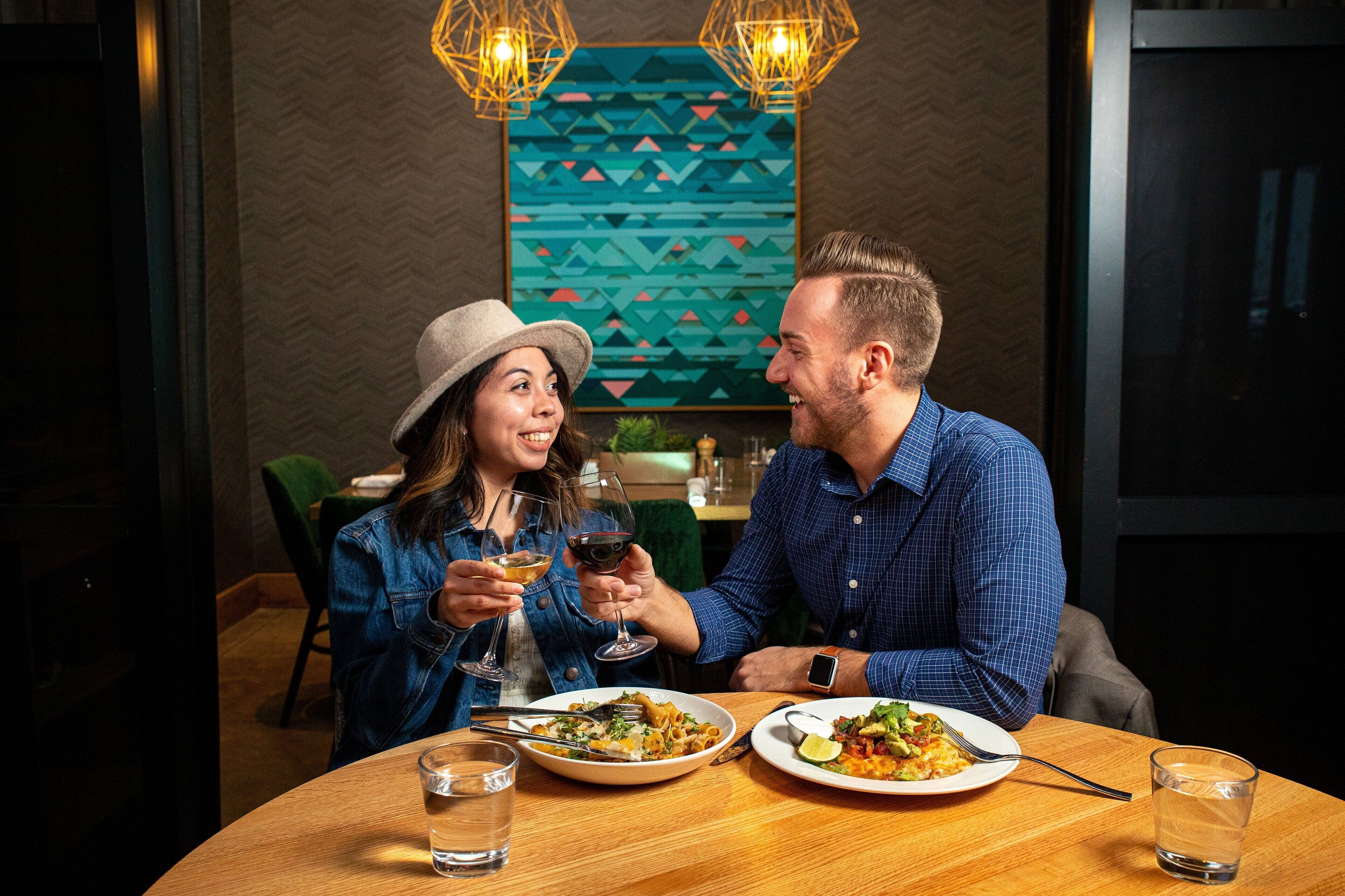 Un couple dînant dans un restaurant décoré d’œuvres d’art géométriques murales, avec une table en bois et un éclairage suspendu.