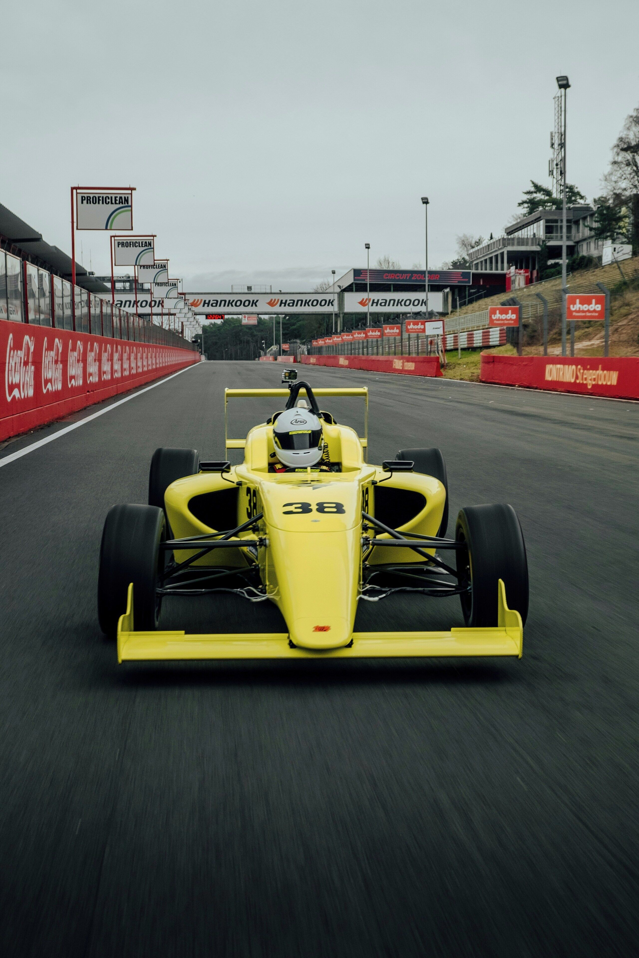 A yellow race car on a track with sponsor logos and a grandstand in the background.
