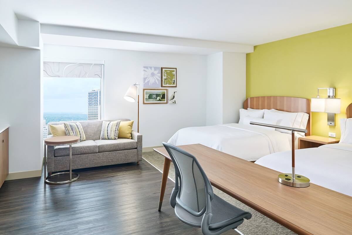 Habitación de hotel con cama, escritorio, sofá y vistas a la ciudad.