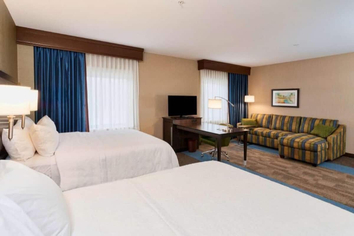 A hotel room with two beds, a TV, a desk, a sofa, and a lamp.
