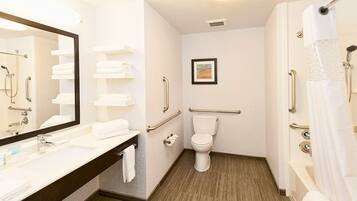 A bathroom with a toilet, a sink with a mirror, a shower, and handrails.