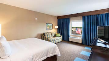 A hotel room with a bed, a sofa, a television, a window with curtains, and a flag outside.