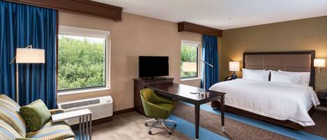 Ein Hotelzimmer mit einem Bett, einem Schreibtisch mit Fernseher, einem Sessel, einer Couch und zwei Fenstern mit Vorhängen.