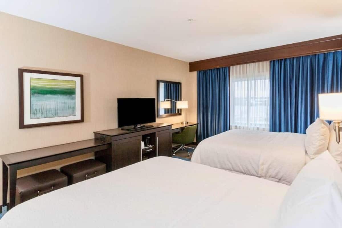 A hotel room with two beds, a desk with a TV, a chair, and a window with curtains.