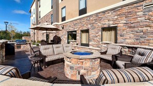 An outdoor patio with stone walls, a fire pit, and striped sofas. - Hampton Inn & Suites Duluth North/Mall Area (Duluth)