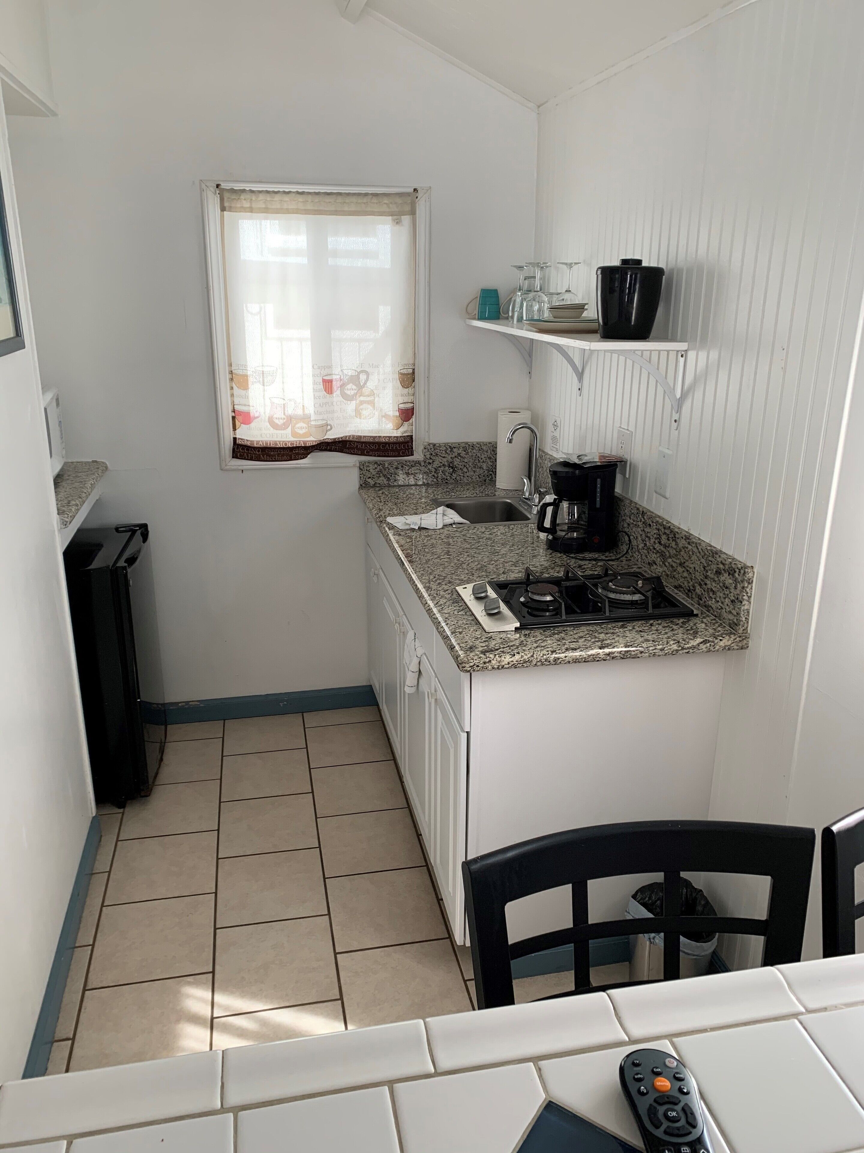 Une cuisine de taille réduite, équipée d’une cuisinière à gaz, d’un évier et d’une fenêtre avec un rideau.