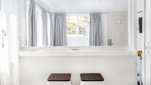 A bathroom with a window, two wooden stools, a ceiling fan, and a white door. - Hermosa Hotel (Avalon)
