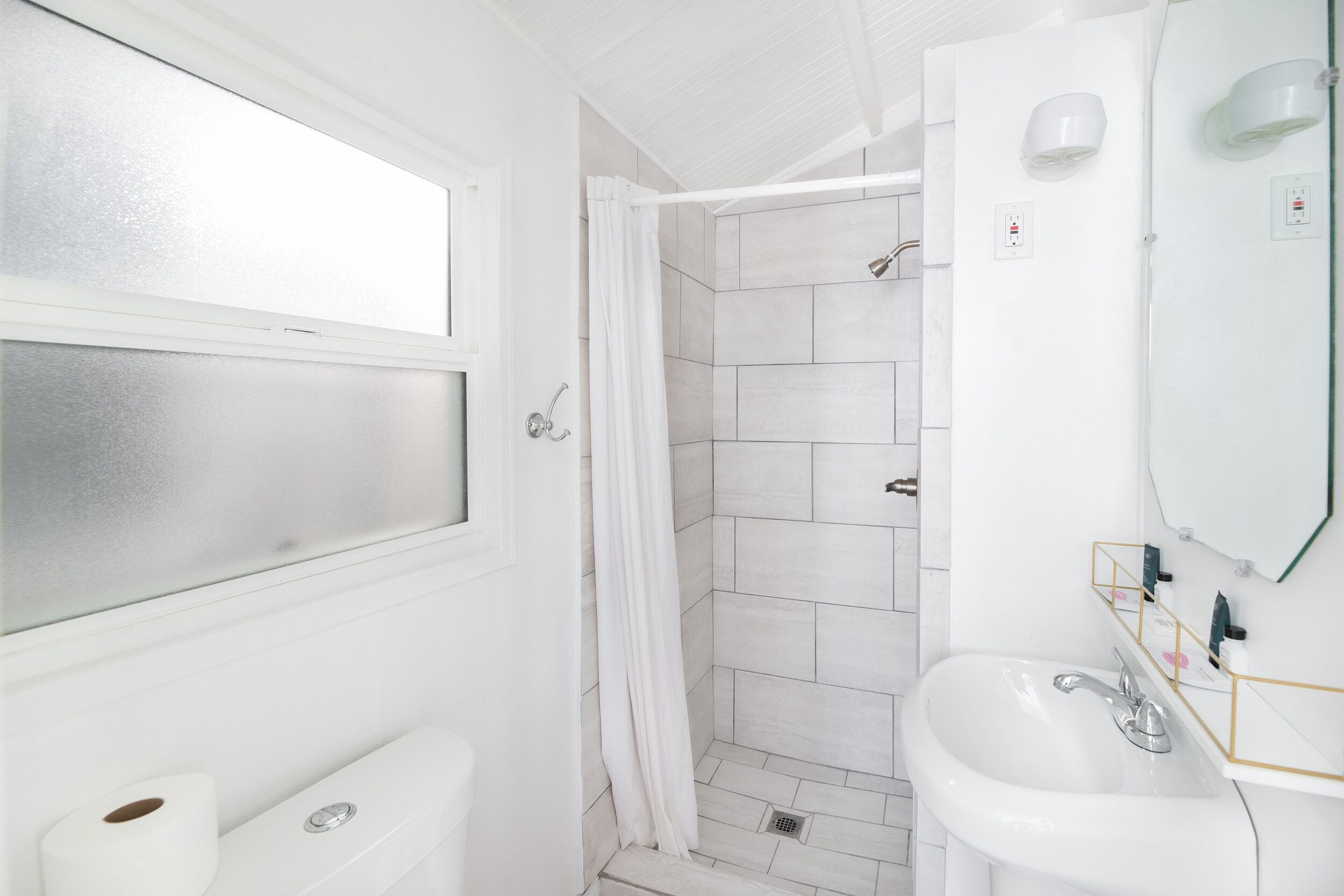 A bathroom with a shower, toilet, sink, and a window.