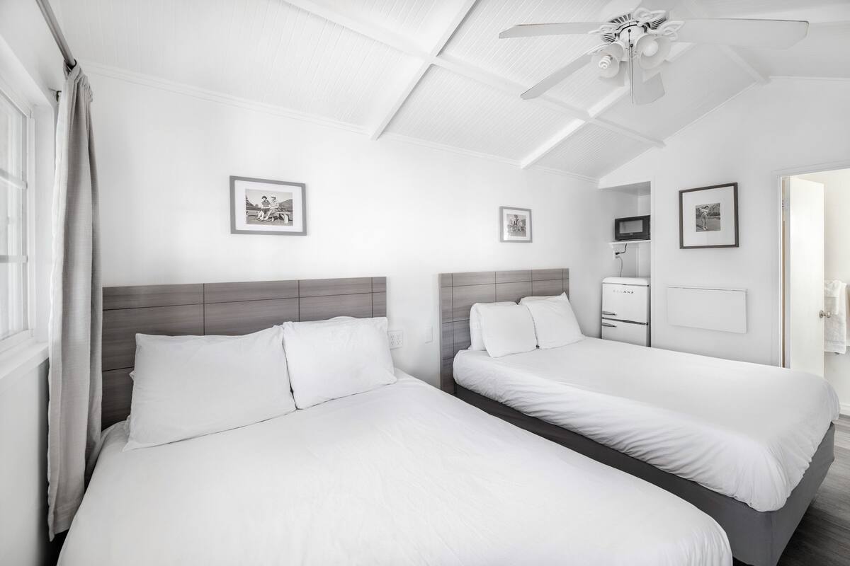 Una habitación de hotel con dos camas, un ventilador de techo y cuadros en las paredes.