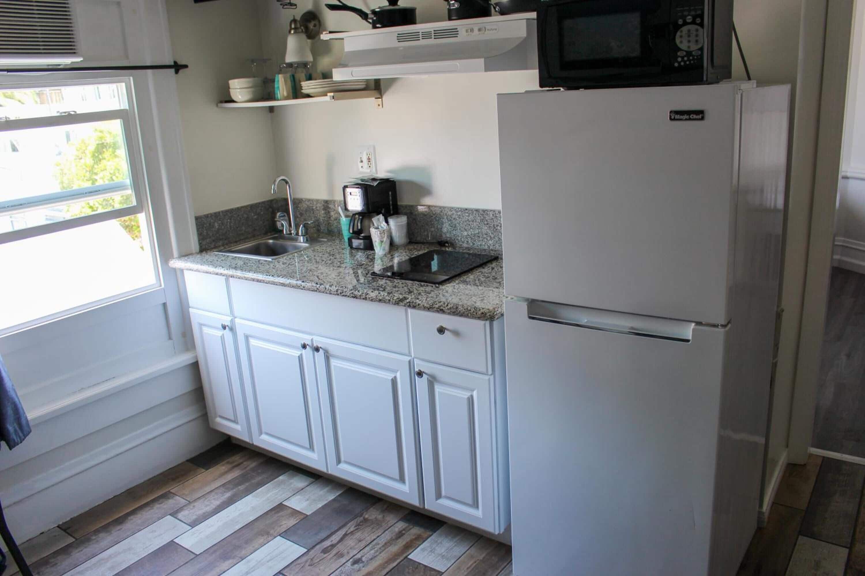 A compact kitchen with white cabinets, a granite countertop, a built-in microwave, and a refrigerator.