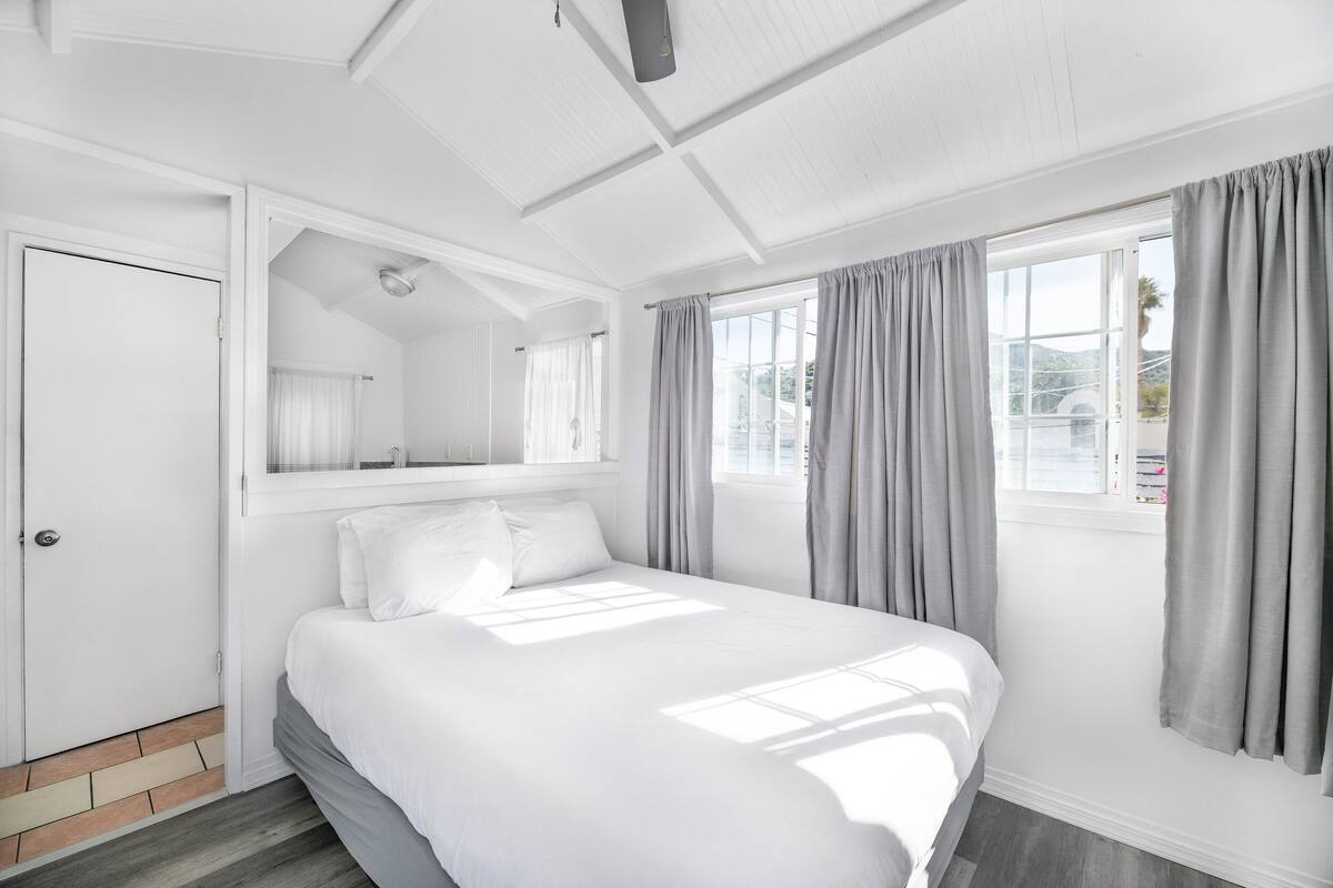 Una habitación de hotel moderna con una cama grande, un armario empotrado, una ventana con cortinas y una lámpara en el techo.