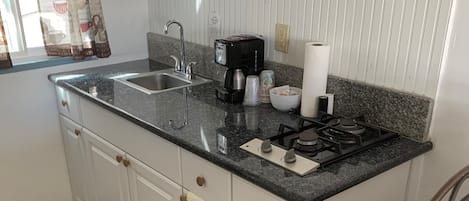A kitchen with a granite countertop, white cabinets, a coffee maker, and a trash bin.