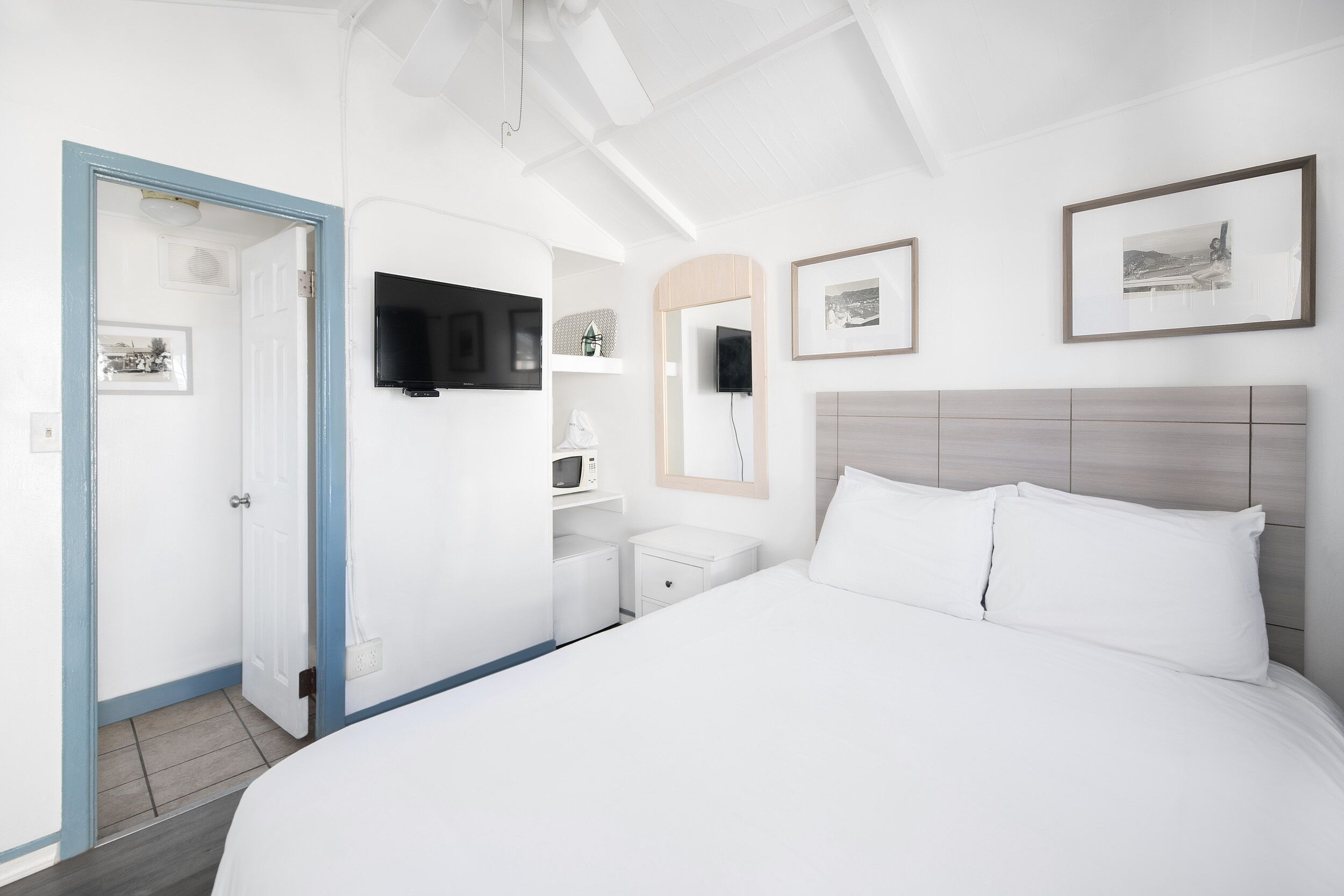 Une chambre d’hôtel avec un grand lit, un téléviseur fixé au mur, une table de chevet et une porte donnant sur une autre pièce.