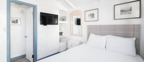 Une chambre d’hôtel avec un grand lit, un téléviseur fixé au mur, une table de chevet et une porte donnant sur une autre pièce.