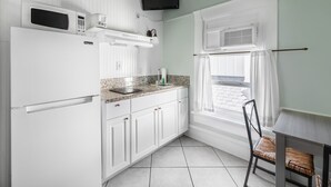 A compact kitchen with white cabinets, a microwave, a built-in oven, a sink, and a window with curtains. - Hermosa Hotel (Avalon)