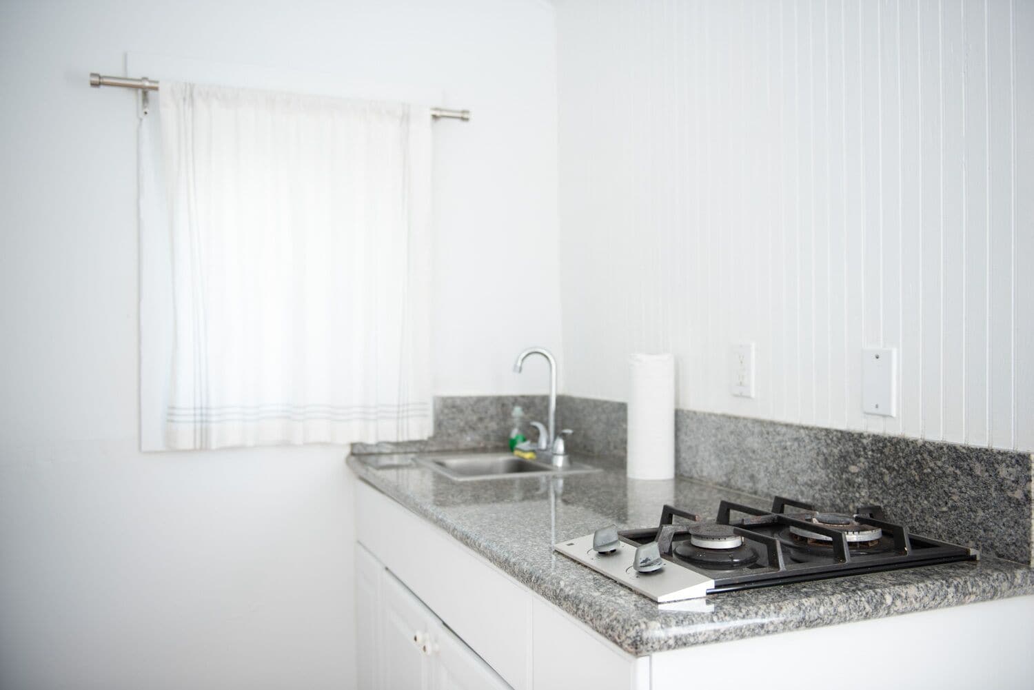 A kitchen with a granite countertop, a gas stove, a sink, and a towel hanging on a rod.