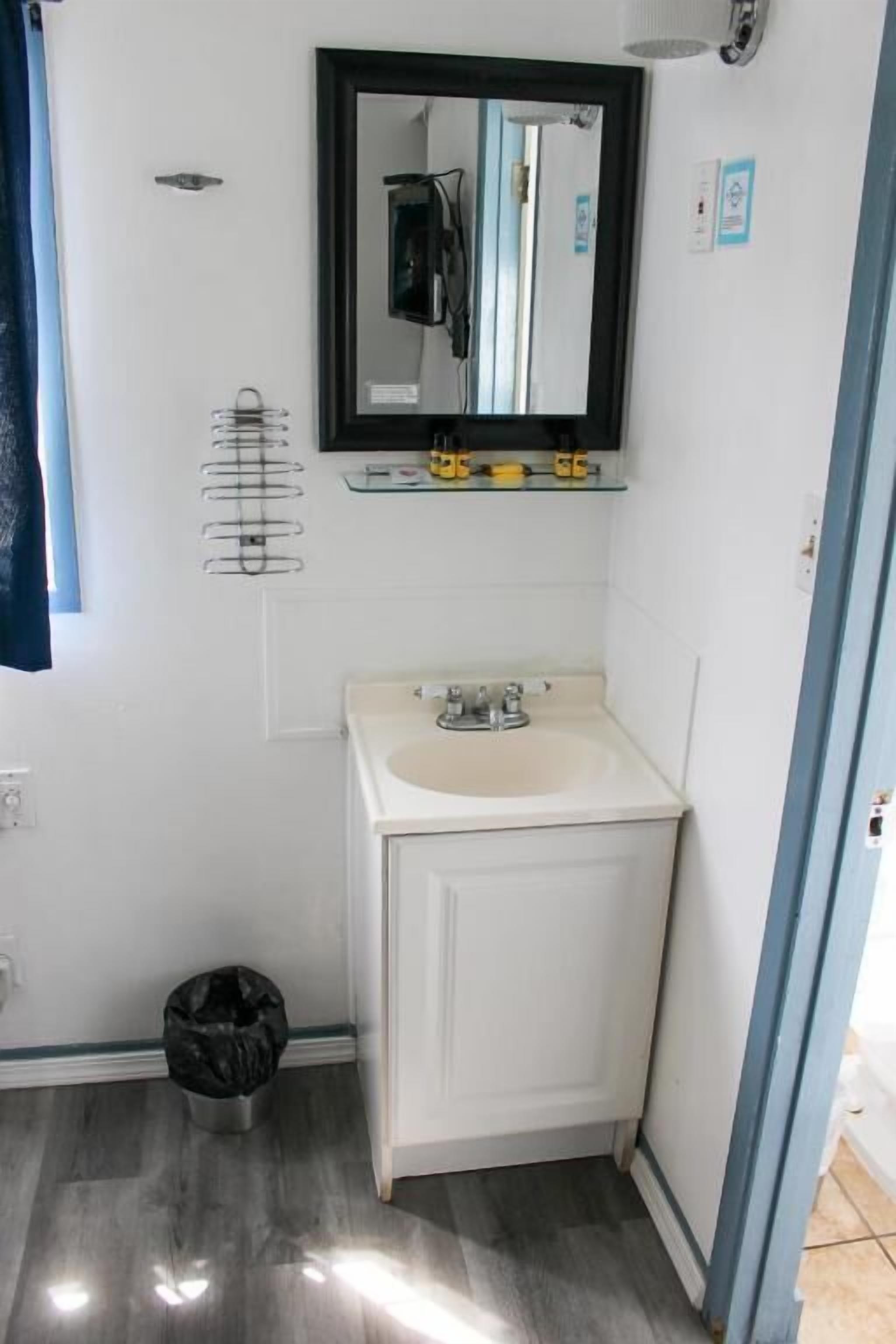 Un baño con un lavamanos blanco, un espejo encima y un cesto de basura negro.