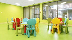 Ein helles Zimmer mit grünen Wänden und einem grünen Boden, ausgestattet mit mehreren bunten Stühlen und Tischen in legerer Anordnung.