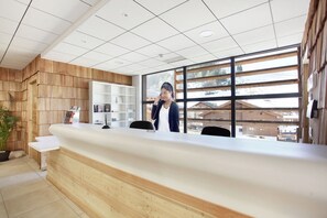 A reception desk with a wooden finish, a potted plant, and a view of a snowy landscape through large windows.