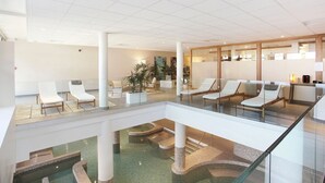 Eine moderne Hotelhalle mit Glasatrium, Lounge-Möbeln und einem Poolbereich.