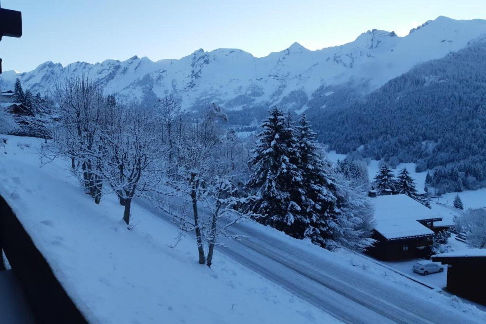 A snowy mountain landscape with a road, trees, and a building.