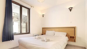 Ein Hotelzimmer mit einem großen Bett, einem Fenster mit Vorhängen, einem Nachttisch und einer Wandleuchte.