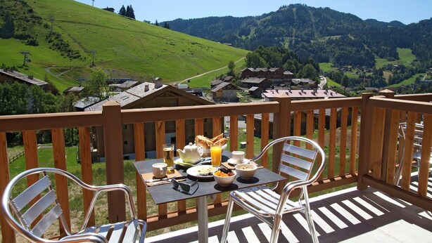 Ein Balkon mit Frühstückstisch, mit Blick auf ein malerisches Dorf und Berge.