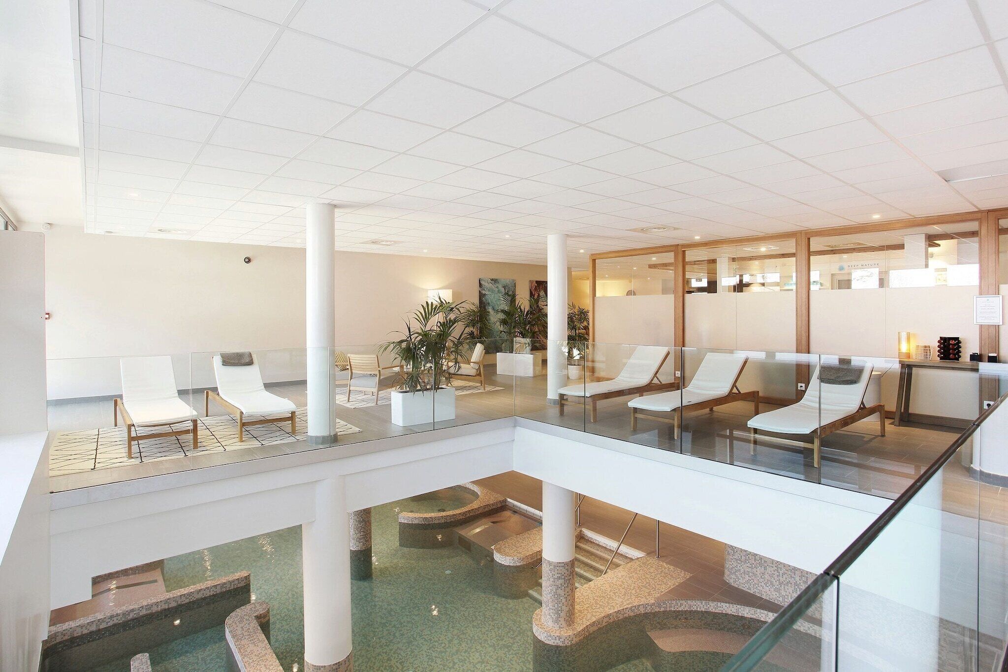 Eine moderne Hotelhalle mit Glasatrium, Lounge-Möbeln und einem Poolbereich.