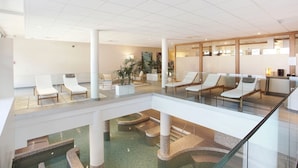 A modern hotel lobby with a glass atrium, lounge chairs, and a pool area. - Chalet in La Clusaz with Pool & Spa (La Clusaz)