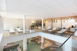 Eine moderne Hotelhalle mit Glasatrium, Lounge-Möbeln und einem Poolbereich.