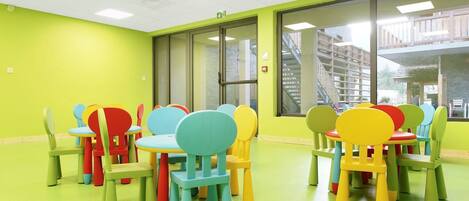A brightly colored room with green walls and a green floor, featuring multiple colorful chairs and tables arranged in a casual setting.