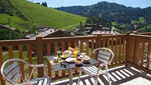 A balcony with a table set for breakfast, overlooking a scenic village and mountains. - Chalet in La Clusaz with Pool & Spa (La Clusaz)