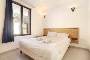 A hotel room with a large bed, a window with curtains, a bedside table, and a wall-mounted light fixture. - Chic Chalet-Style Apartment (La Clusaz)