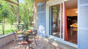 A covered patio with a table set for dining, a sliding glass door leading to a kitchen, and a view of greenery outside. - Holiday Home in Corsica by the Sea (Poggio Mezzana Corse)