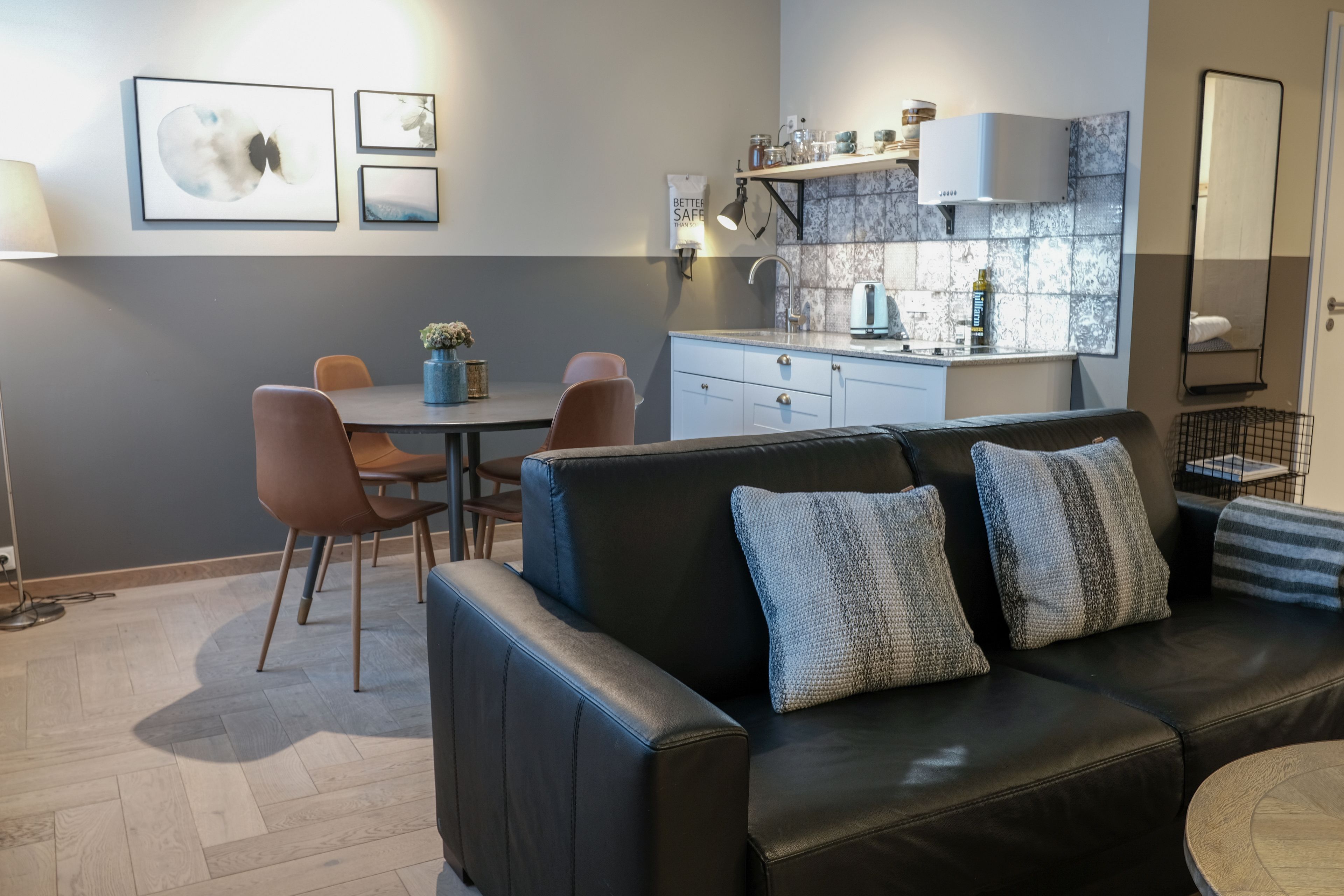 A modern living room with a black leather sofa, a dining table with chairs, and a kitchen area with a countertop and cabinets.