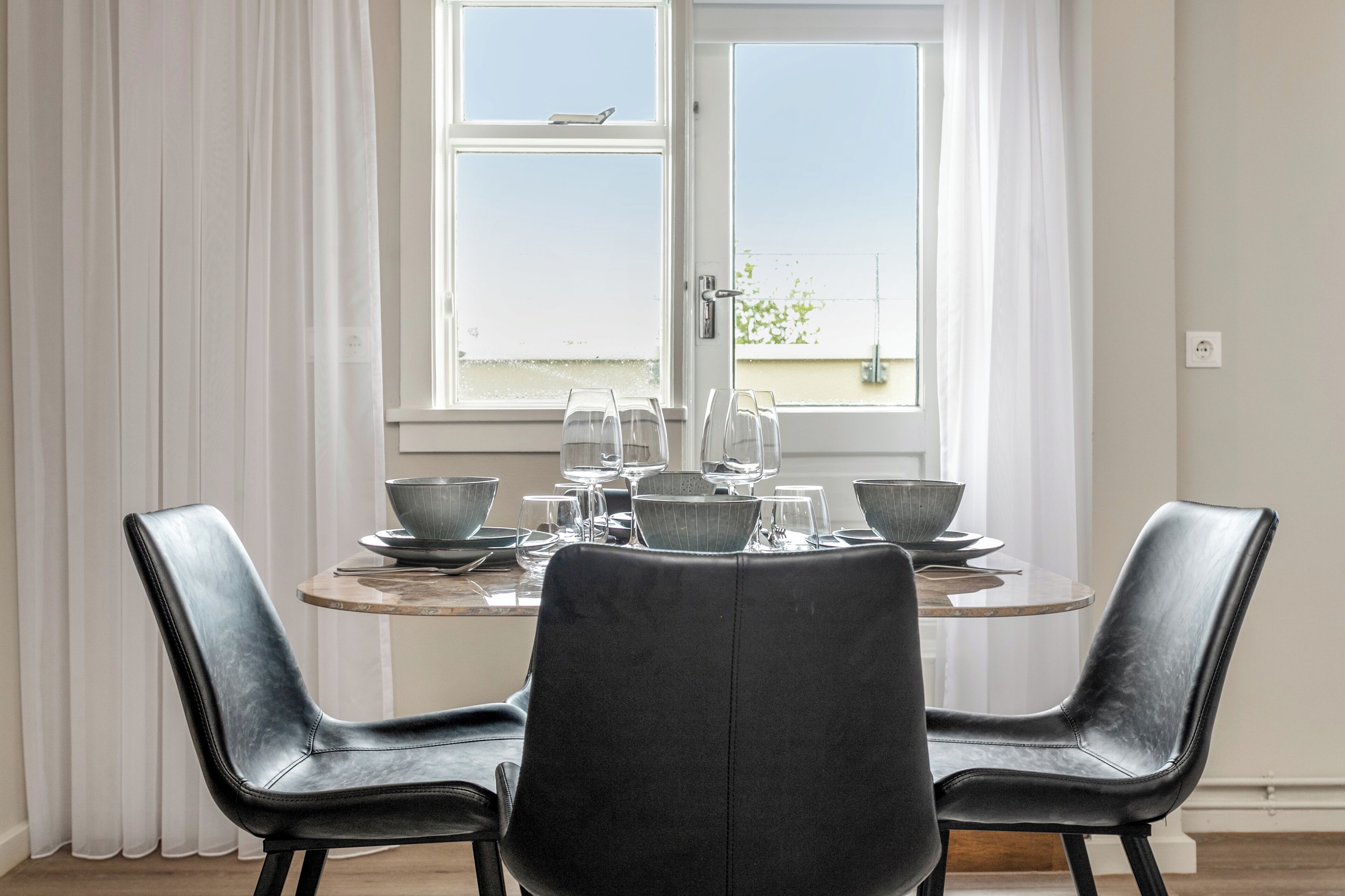 A dining area with a table set for four, two black chairs, and a window with curtains.