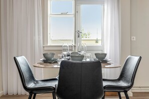 A dining area with a table set for four, two black chairs, and a window with curtains. - The Swan House by Heimaleiga (Reykjavik)