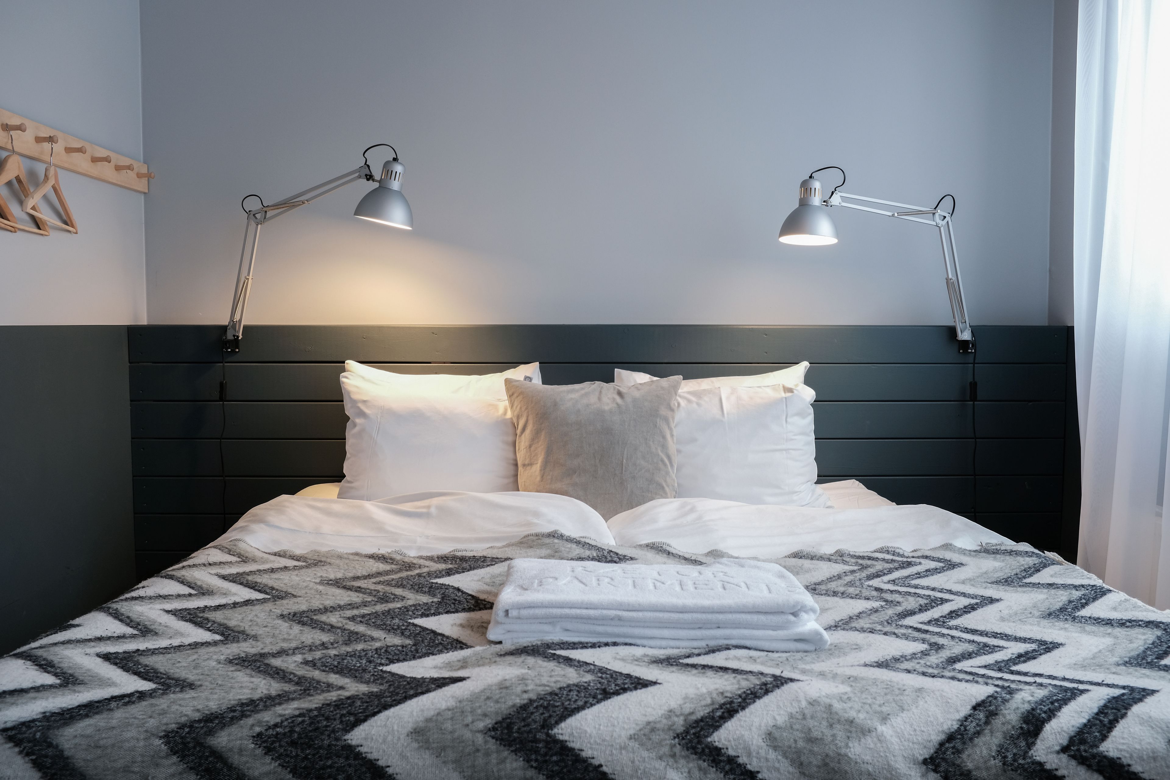 A neatly made bed with two bedside lamps, a patterned blanket, and a folded towel on the bed.