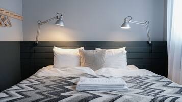 A neatly made bed with two bedside lamps, a patterned blanket, and a folded towel on the bed.