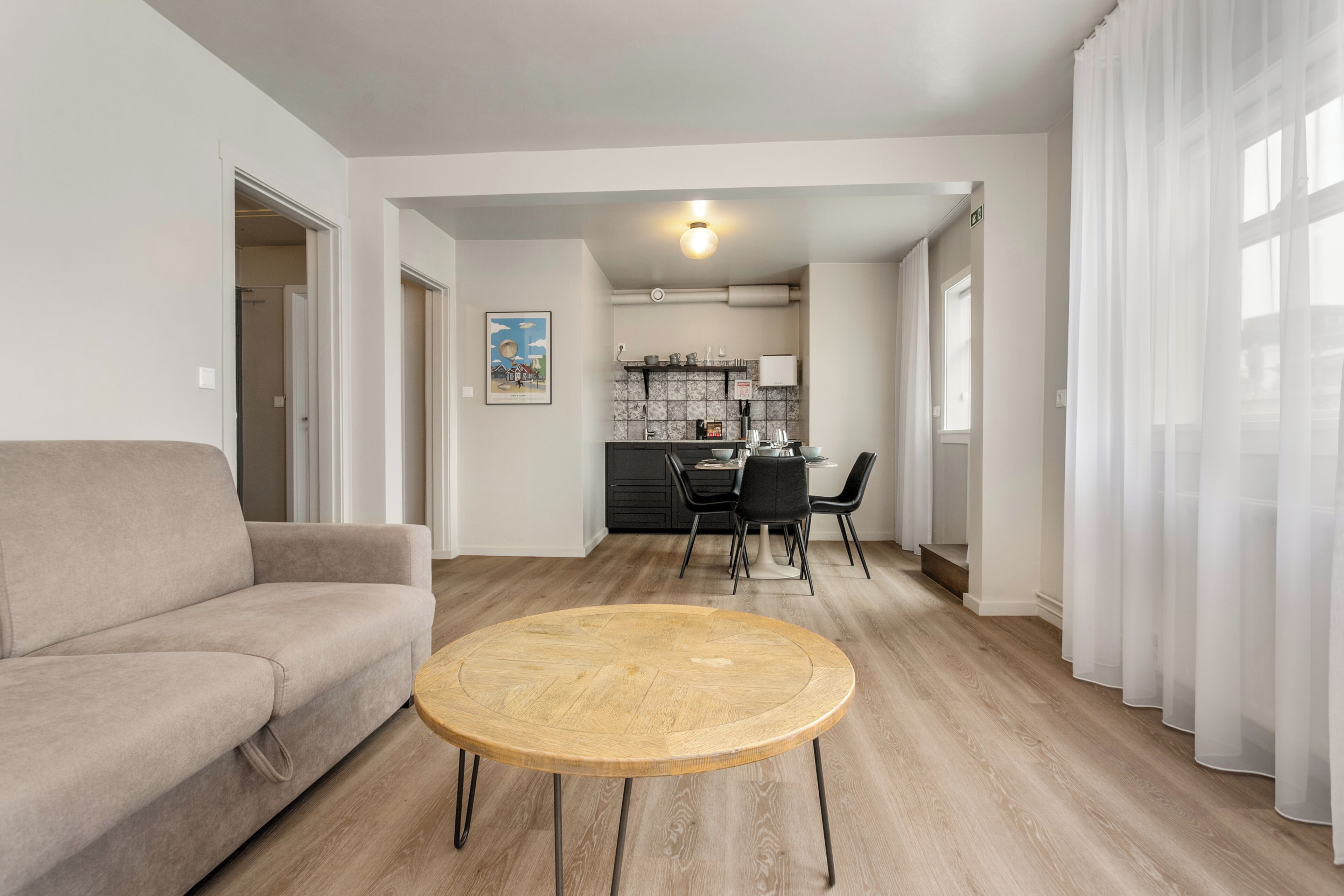 A modern living room with a sofa, a round wooden table, and a kitchen in the background.