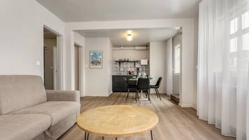A modern living room with a sofa, a round wooden table, and a kitchen in the background.